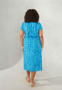 Blå leopardmönstrad maxikjol med korta ärmar, dragsko i midjan och flödande tyg, tillsammans med beige kilklackar. Enkel, avslappnad design.