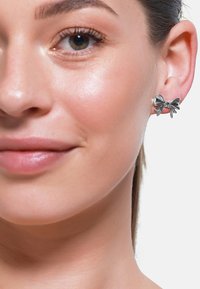 Silberne, bogenförmige Ohrringe mit polierter Oberfläche. Das Design ist kunstvoll mit einem zentralen Knoten und fließenden Schleifen.
