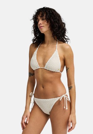 Set de bikini croșetat în culoarea alb-crem, cu un top triunghiular cu bretele subțiri și chiloți cu șnururi laterale ajustabile. Design tricotat texturat.