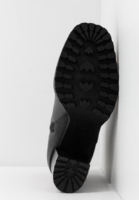 Musta nahkaboot, jossa on kestävä, teksturoidun kumipohjan syvät urat ja hieman kalteva muoto.