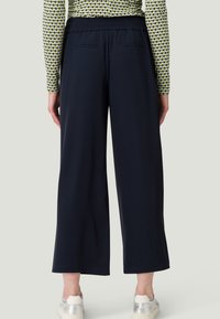 Marineblauwe wijde broek met een elastische tailleband, voorzien van twee achterzakken en een soepele textuur. Geschikt voor casual dragen.