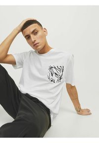 Hvid kortærmet t-shirt med en sort blomstertrykt lomme. Blødt stof, afslappet pasform, parret med sorte bukser. Enkel og moderne design.