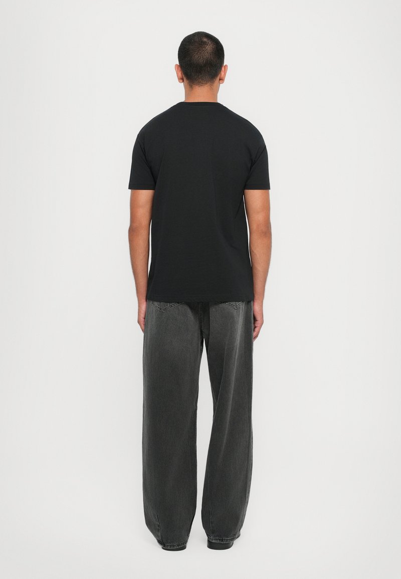 T-shirt noir à manches courtes, design col rond, porté avec un jean gris foncé ample. Simple, couleur unie avec un minimalisme dans les détails.