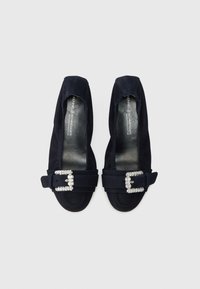 Mornarsko plave cipele od brušene kože s zatvorenim vrhom i ukrasnim kopčom na remenu. Glatki, ravni potplat sa blagom teksturom.