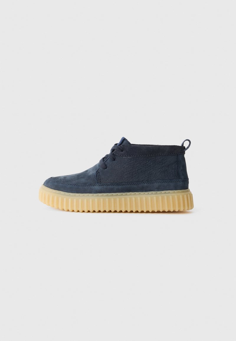 Navy blue suede ankle boot with front laces, a textured finish, and a beige rubber sole featuring ridges for traction.