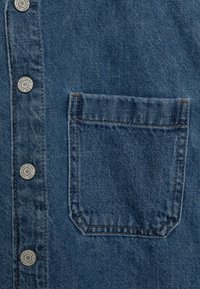 Blue denim fabric with a stitched chest pocket and metal snap buttons labeled "GAP DENIM EST. 1969" on the left side.