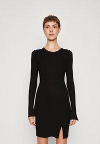 Robe noire à manches longues rainurées avec un col rond et une fente à l'ourlet, présentant une silhouette ajustée et un tissu texturé.