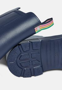 Plave gumene čizme za kišu s teksturiranim potplatima i šarenom prugastom petljom za povlačenje. Imaju glatku gornjište i uzorak na potplatu za bolju prionljivost.