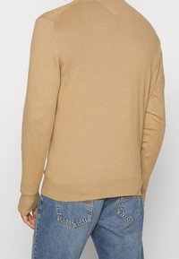 Pull beige en maille côtelée avec manches mi-longues, col ras du cou et coupe décontractée. La vue arrière montre un design épuré sans marque visible.