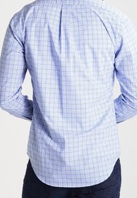 Rutigt skjorta i ljusblått och vitt, gjort av bomull. Har en veck bak, långa ärmar och en skräddarsydd passform.