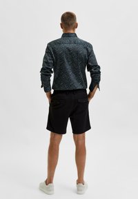 Černá košile s multicolor vzorem teček, dlouhými rukávy a límcem na knoflíky, v kombinaci s černými šortkami a bílými teniskami.