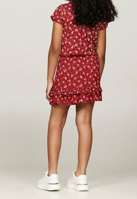 Rotes Blumen Kleid mit kurzen Ärmeln, gerüschtem Saum und weißen Sneakers. Leichter Stoff, mit verstreuten Blumenmustern.
