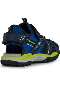 Sandalias azul y marino con parte superior de malla transpirable, correa ajustable, acentos en verde lima y suela texturizada. Diseño ligero y resistente al agua.