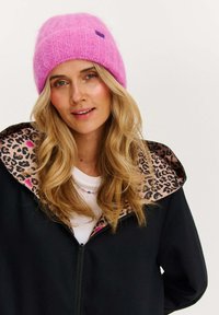 Ružová pletená čiapka s rebrovanou štruktúrou. Čierna bunda s leopardím vzorom na vnútornej podšívke a biele tričko pod ňou.