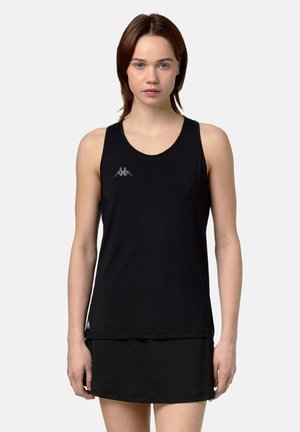 Giovane donna con capelli castani lisci che indossa un top nero senza maniche e una gonna abbinata, di fronte a uno sfondo semplice.