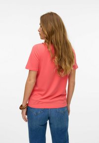 Korala bluzka z krótkim rękawem, wykonana z miękkiego materiału, z okrągłym dekoltem. W zestawie z luźnymi niebieskimi dżinsami, charakteryzującymi się swobodnym krojem i widokiem z tyłu.