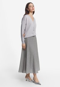 Ljusgrå, långärmad V-ringad topp som bärs tillsammans med en plisserad silvergrå midikjol. Modellen har på sig skinande silverfärgade slingback-klackar.