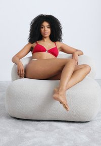 Buet, overdådig cremefarvet polstret stol med tekstureret overflade, med et bredt, rundt design. En person sidder afslappet iført en rød bikini.