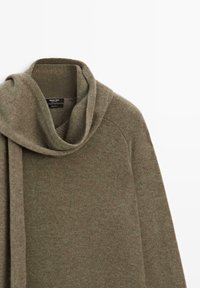 Khaki gebreide trui met een gedrapeerde sjaalkraag en zachte textuur. Heeft raglanmouwen en een minimalistisch label aan de binnenkant.