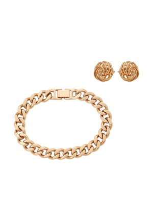 Bransoletka z ogniw łańcucha w złotym odcieniu z prostokątnym zapięciem oraz pasujące złote kolczyki w kształcie skręconych węzłów na białym tle.