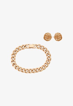 Goudkleurige armband met schakels en rechthoekige sluiting, gecombineerd met bijpassende goudkleurige oorstekers in de vorm van gedraaide knopen, op een witte achtergrond.