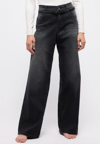 Schwarze, weit geschnittene Jeans aus Denim mit einem hohen Bund und Gürtel, sowie zwei vorderen Taschen. Glatte Textur mit dezenten Ausbleichungen.