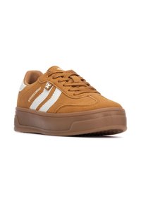 Zapatilla de ante marrón con una suela de goma gruesa, que presenta rayas blancas y detalles del logo. Diseño de cordones y acolchado en el collar para mayor comodidad.