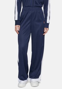 Pantaloni da jogging navy a righe con pannelli laterali bianchi, vita elastica e polsini affusolati. Realizzati in tessuto morbido e leggero.