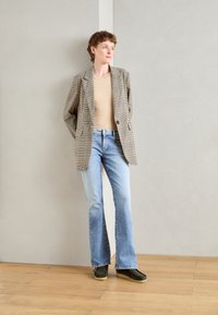 Checkered blazer in beige and brown, fitted tan top, light blue flared jeans, and dark green shoes on wooden floor against light gray background.
