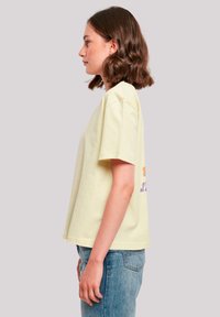 Yellow cotton t-shirt with short sleeves, relaxed fit, featuring colorful text graphics on the back, paired with blue denim jeans.