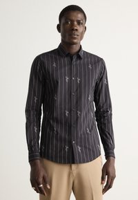 Camicia nera con bottoni, a righe verticali bianche e motivi ricamati. Maniche lunghe e design slim fit. Tessuto di tessitura liscia.
