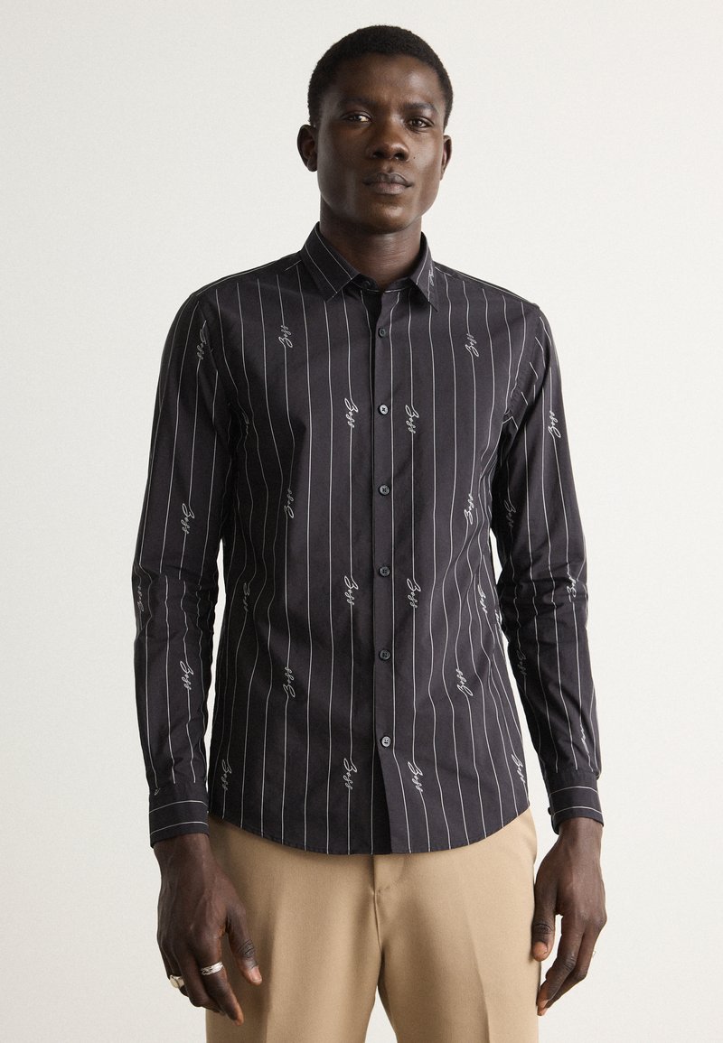 Camicia nera con bottoni, a righe verticali bianche e motivi ricamati. Maniche lunghe e design slim fit. Tessuto di tessitura liscia.