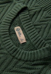 Zielony sweter dzianinowy z prążkowanym okrągłym dekoltem, ozdobiony fakturowanym wzorem oraz beżową metką zawierającą informacje o marce i rozmiarze.