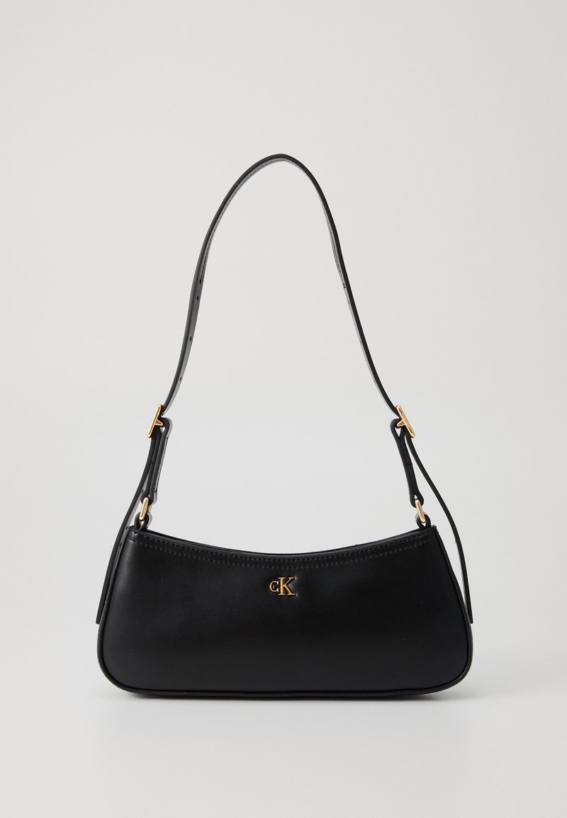 Bolsa de couro preta com um design curvado, apresentando uma única alça de ombro e um logo dourado "cK" na parte frontal. Textura suave e estilo minimalista.