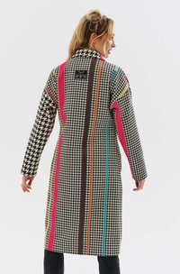 Długi płaszcz z wzorem w jodełkę w czerni i bieli, akcentowany kolorowymi pionowymi pasami w różowym, brązowym, pomarańczowym i turkusowym.