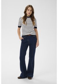 Pasiasty, krótki top w kolorze granatowym i białym, noszony z ciemnoniebieskimi rozkloszowanymi dżinsami z kontrastowym przeszyciem i bocznymi rozcięciami, w połączeniu z butami.