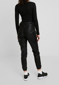 Černé kožené cargo kalhoty s tapered nohavicemi, elastickými manžetami a zadními kapsami. Nosené s upnutým černým topem s dlouhým rukávem a černými teniskami.