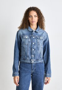 Chaqueta de denim en azul claro con cuello clásico, cierre de botones, dos bolsillos en el pecho y mangas largas. Textura suave y corte cropped.