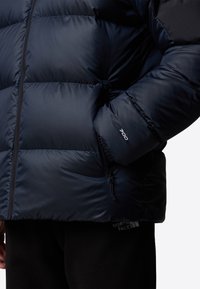 Marinblå pufferjacka med quiltad textur, hög krage, dragkedjefickor och "700"-logotyp på ärmen. Mjuk tyg och isolerad design.