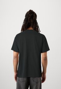 Svart bomullströja med rund nacke och korta ärmar, sedd bakifrån. Lös passform med en mjuk yta och inga synliga mönster.