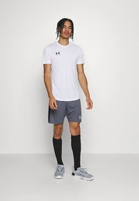 Meeste spordirõivastus, mille moodustavad valge lühikeste varrukatega särk, hallid lühikesed püksid, mustad põlveni ulatuvad sokid ning hallid spordijalatsid. Särgil ja lühikestel pükstel on nähtav logo.