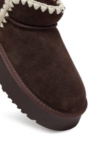 Bruine suède enkelboot met een ronde teen, crèmekleurige stiksels langs de kraag en een gestructureerde donkerbruine zool.