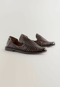 Zapatos de piel trenzada en marrón, tipo slip-on, con punta abierta, que cuentan con una superficie lisa, suela plana y un diseño redondeado para mayor comodidad.