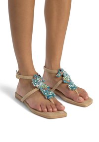 Sandalias de dedo beige con suelas planas, que presentan un conjunto decorativo de cuentas azules y de varios colores a lo largo de las correas.