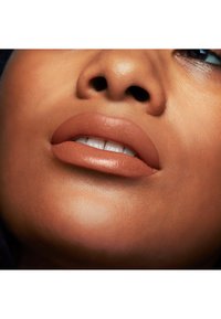 Rouge à lèvres nude mat appliqué sur des lèvres pulpeuses, sur un teint lisse avec une légère éclat, mettant en avant un look naturel et soigné.