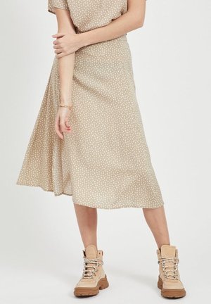 Gonna midi beige a pois in tessuto leggero con un design svasato, abbinata a stivali tan con lacci e suola spessa.