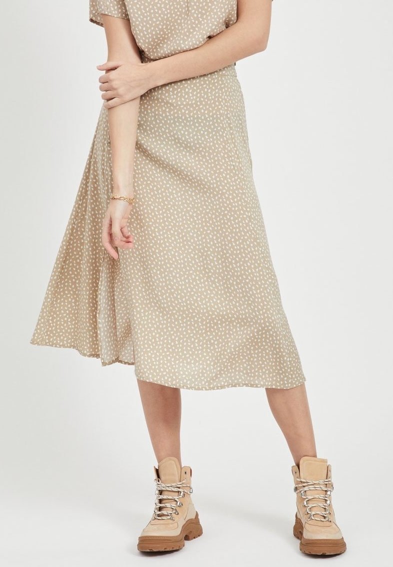 Jupe midi beige à pois en tissu léger avec un design évasé, associée à des bottes à lacets beiges avec une semelle épaisse.