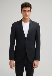 Marineblazer met twee knopen, notch revers en twee voorzakken. Gedragen boven een wit T-shirt, met een gestructureerde stof en een gladde afwerking.