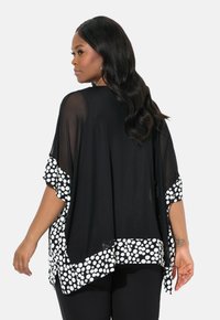 Průsvitný černý kimono-styl top s bílými puntíky na rukávech a spodním lemu, s volným střihem a splývavou tkaninou pro pohodlí.