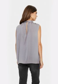 Blusa grigia senza maniche in tessuto leggero e liscio con scollatura arricciata e chiusura a oblò sul retro. Presenta una vestibilità morbida e un design minimal.